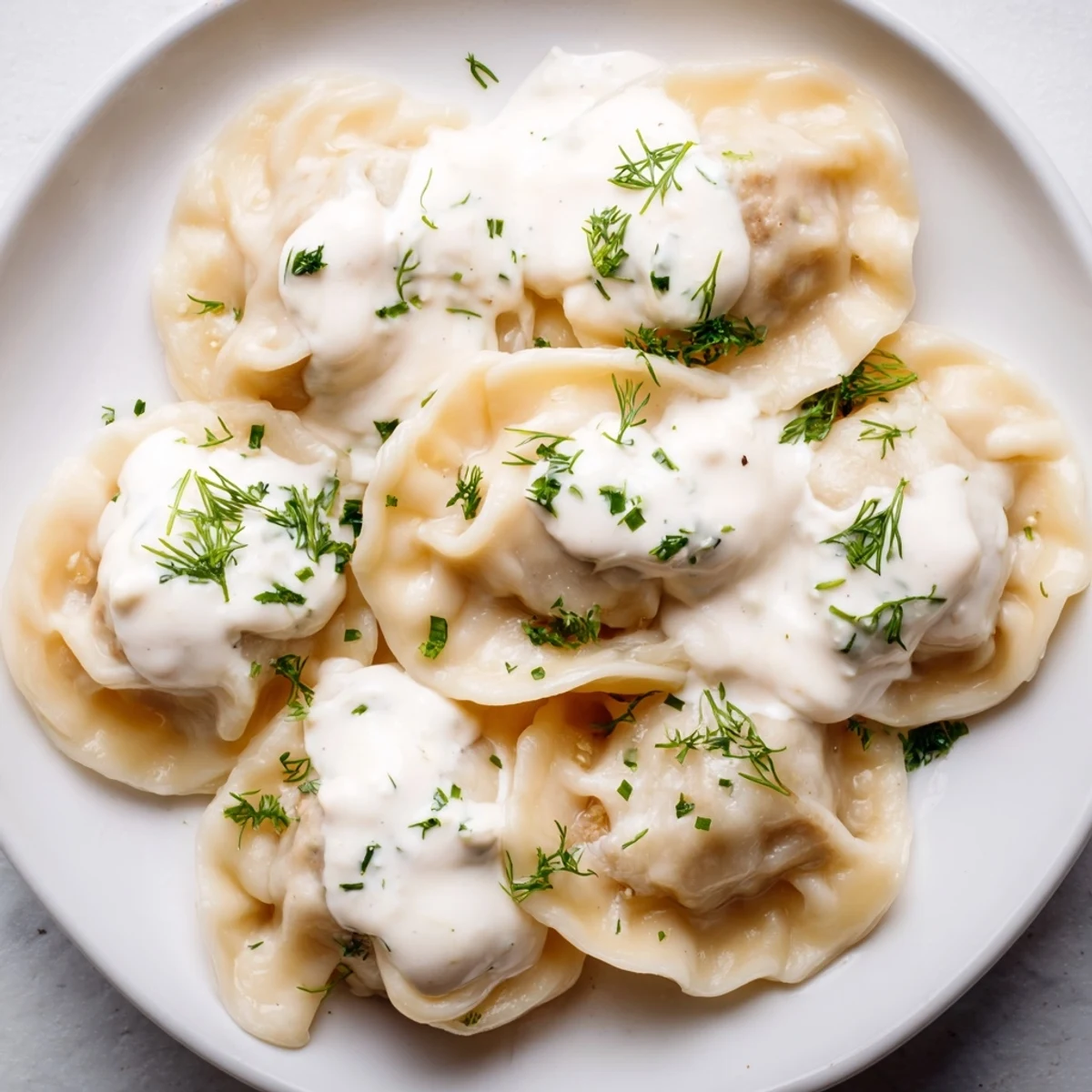 Golden, tender Russian Pelmeni, a comforting bowl of dumplings with a swirl of sour cream.