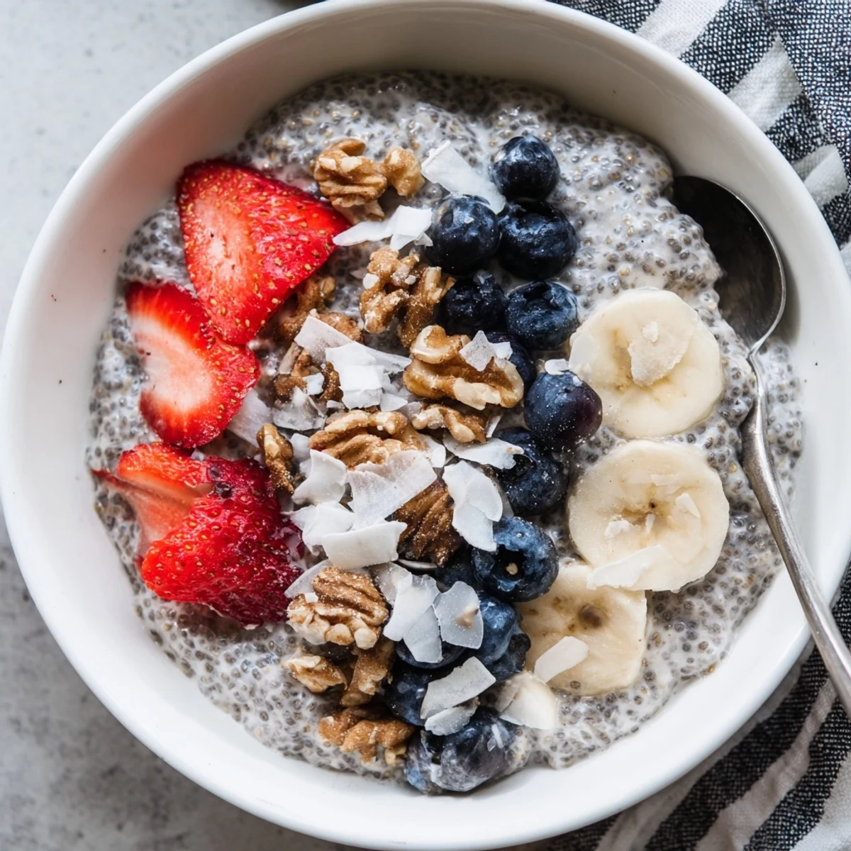 Creamy chia seed pudding in glass jars, topped with fresh berries, sliced banana, and shredded coconut for a healthy breakfast or snack.