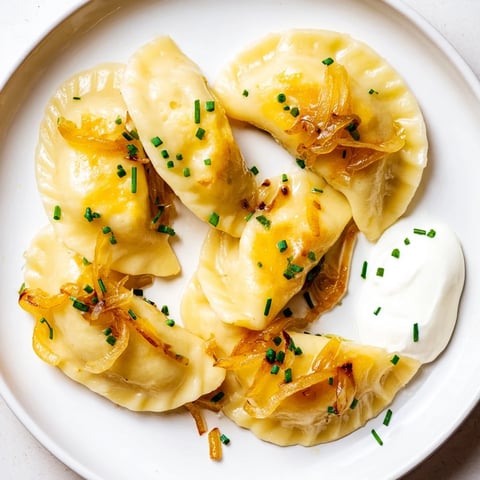 Golden-brown pan-fried Polish pierogi dumplings are served with sweet caramelized onions and sour cream.