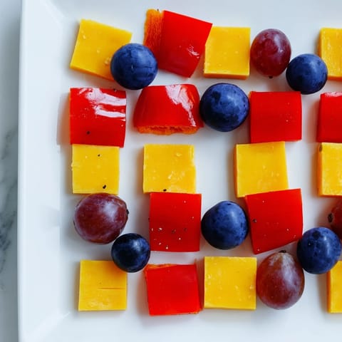 Colorful Bauhaus Block appetizer with cheddar, red pepper squares, and juicy grapes; a party favorite.