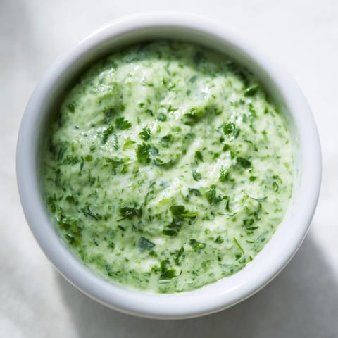 In a bright kitchen, creamy green goddess dressing is drizzled over a colorful mixed green salad for dinner.