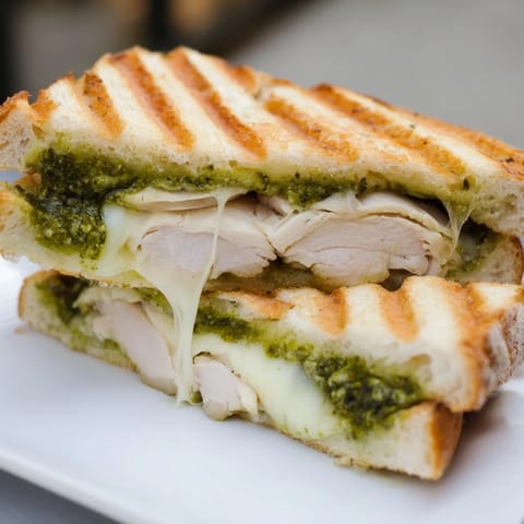 Warm, crusty ciabatta halves cradle vibrant basil pesto and tender sliced chicken in this close-up Chicken Pesto Panini. 