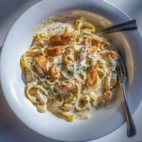 A fork lifts a bite of spicy Cajun chicken Alfredo, showcasing the silky, cheesy sauce clinging to pasta noodles.