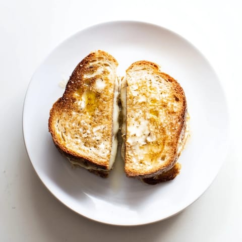 A close-up of a crispy Truffle Grilled Cheese, featuring generous layers of melty Gruyère and a drizzle of truffle oil on toasted artisan bread.