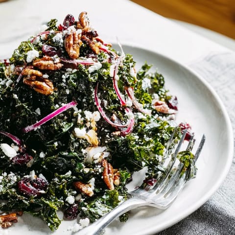 Vibrant massaged kale salad topped with dried cranberries, toasted pecans, and crumbled feta in a warm maple mustard dressing.  