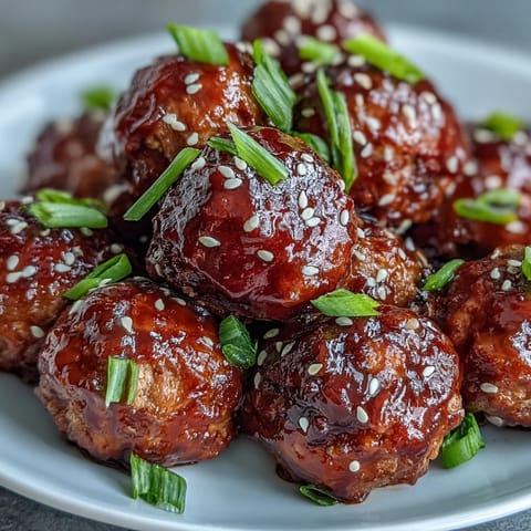 Golden-brown Spicy Chili Honey Turkey Meatballs glistening with a sticky sweet glaze on a white plate, garnished with green onions.