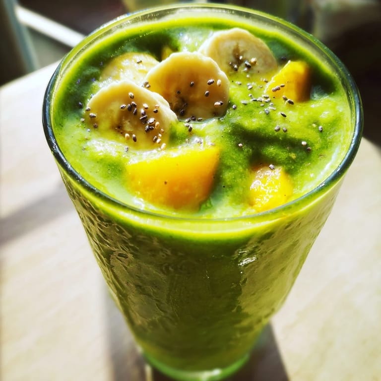 A vibrant glass of Spinach-Hidden Smoothie topped with a sprinkle of chia seeds and sliced banana.