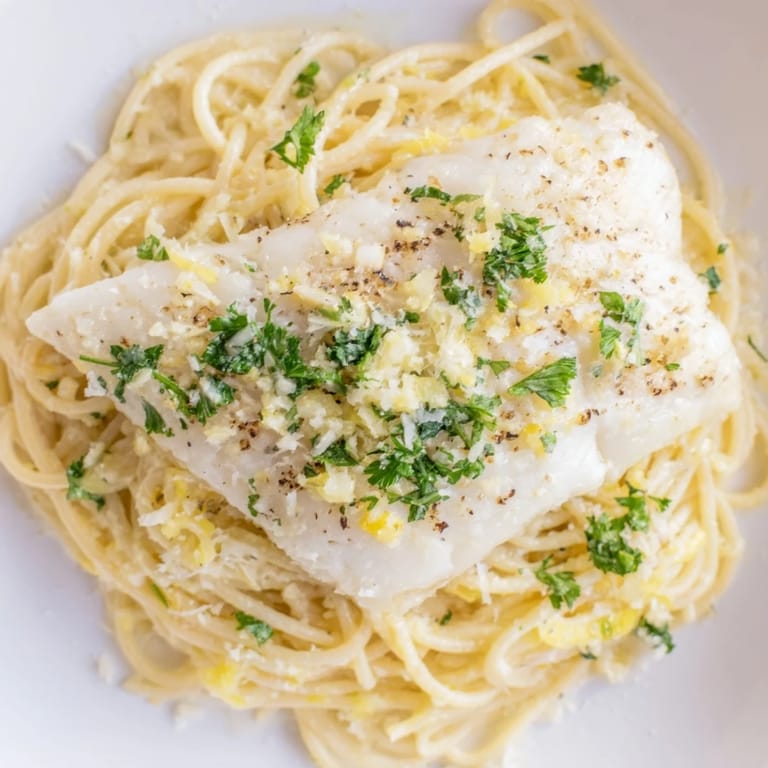 A vibrant serving of Lemon Bass Pasta with tender fish, garlic aroma, and bright lemon wedges for a fresh Italian-inspired meal.