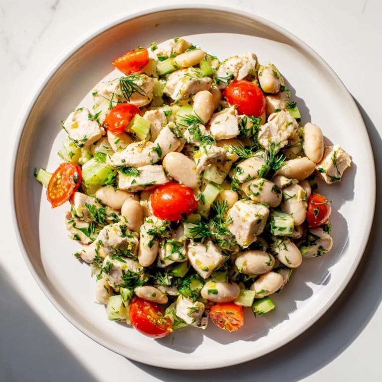 A bright overhead shot of Lemony White Bean Chicken Salad served on a wood table, garnished with dill and lemon wedges next to crusty bread.