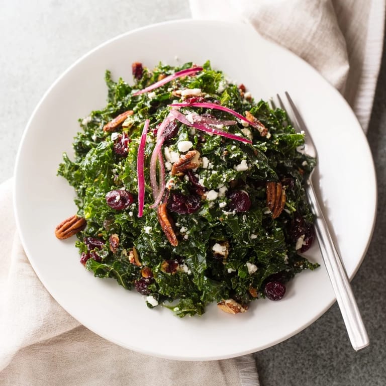 A close-up view of a warm kale salad with maple mustard glaze, sliced red onion, and crunchy toasted walnuts.  