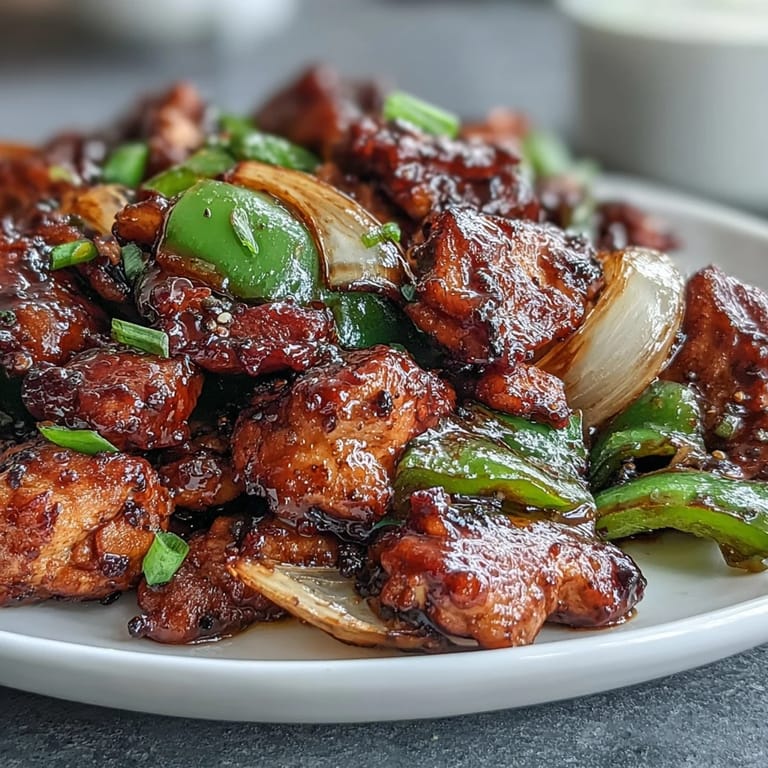 A wok holds sizzling Black Pepper Chicken with sliced onions, ready to be served over steamed rice.