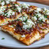 Crispy golden flatbread topped with sweet caramelized onions and creamy goat cheese, garnished with fresh thyme and a hint of balsamic glaze.